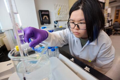 Student works in the lab adding items to a piece of equipment