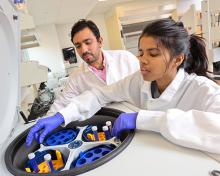 Student views tubes in centrifuge while professor looks on