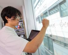 Student draws formulas on the window while holding laptop